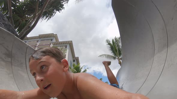 A boy plays on a waterslide water slide in a pool at a hotel resort. alt