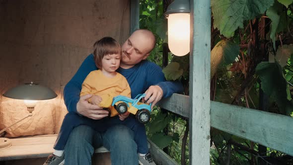 Father is Playing on Porch of the House with His Cute Little Child in a Toy Car