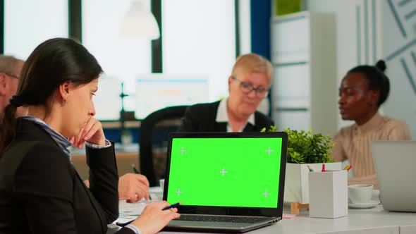 Over the Sholder of Manager Sitting at Meeting Desk Looking at Laptop with Green Screen alt