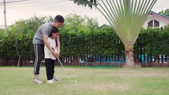 Asian young father training his daughter to play golf on the behalf of the grass on vacation alt