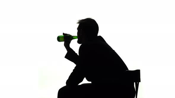 Alcoholic Sits with a Bottle in His Hands and Drinks. Side View. Silhouette White Background alt