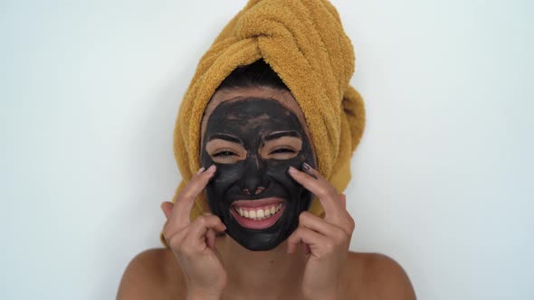 Young smiling woman applying facial charcoal mask portrait alt
