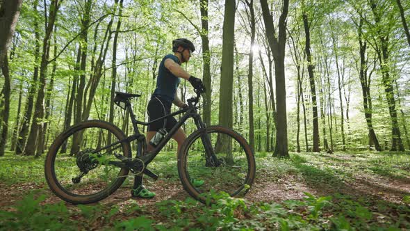A Happy Man with a Bicycle is Walking Along a Forest Path alt