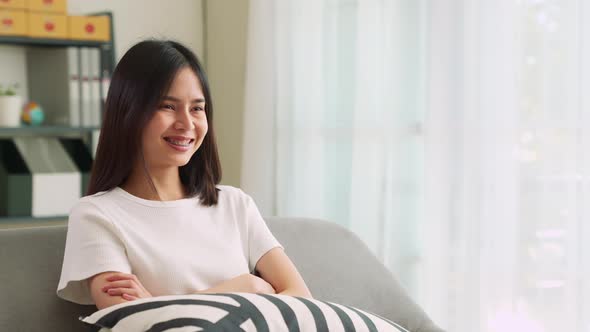 Woman sitting at the sofa in the house and holding the TV remote to watch movies alt