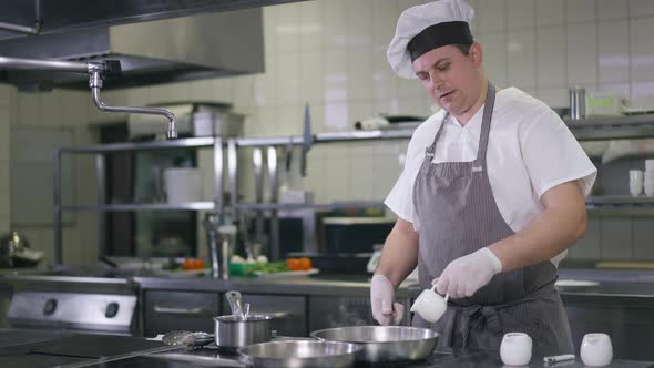 Medium Shot Confident Professional Cook in Chef Hat Pouring Water in Pan Frying Dinner in Restaurant alt