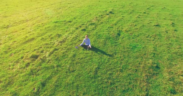 Low Orbital Flight Around Man on Green Grass with Notebook Pad at Yellow Rural Field. alt