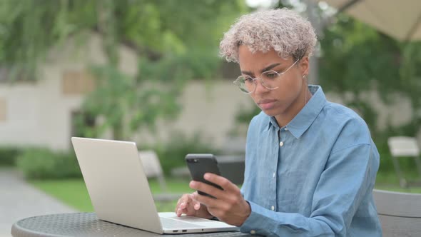 Attractive Young African Woman Using Smartphone in Outdoor Cafe alt