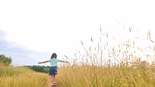 Happy Little Girl Runs Among the Tall Grass in a Field in Summer