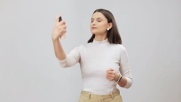 Woman In Beige Outfit Sprays Moisturising And Makeup Fixing Product On Her Face