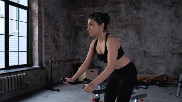 A beautiful athletic young brunette woman in sportswear trains on a sycle in the gym