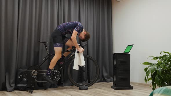 Man hard pedaling out of saddle and intense cycling on home smart trainer indoor. Cycling concept alt