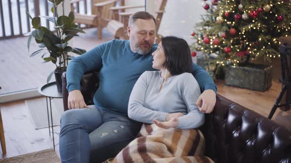 Top Angle View of Relaxed Caucasian Husband and Wife Sitting on Couch and Talking on Christmas Eve alt