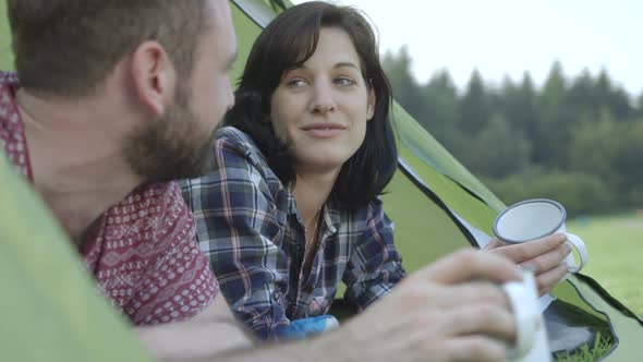 Couple lying in dome tent and drinking coffee