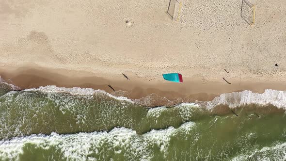 AERIAL: Top View Shot of People Walking on a Beach and Surfers Kite Waving in Wind