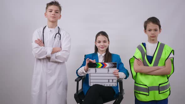 Positive Confident Little Producer Sitting on Chair with Clapping Board As Friends in Doctor and alt