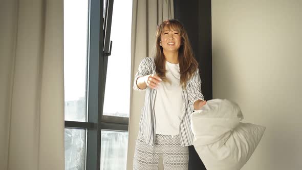 Young Asian Woman Standing on the Bed Cheerfully Throws Pillows Up