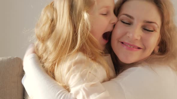 Cute adorable funny little kid daughter tickling caressing young mum kissing on cheek playing on sof