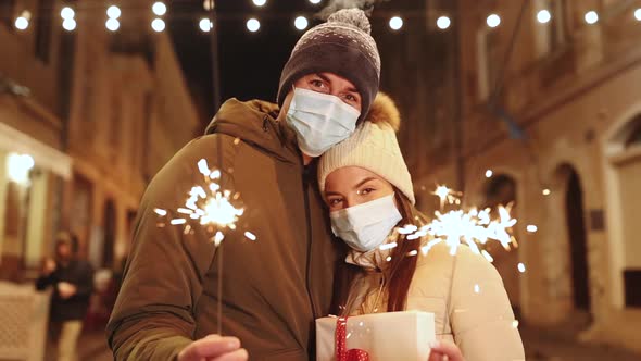 Beautiful Couple in Protective Medical Masks Standing on the Street Holding Sparklers