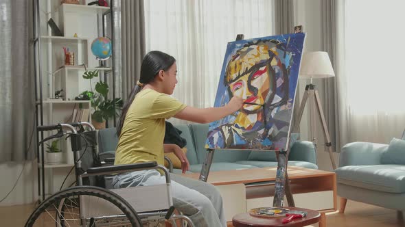 Side View An Asian Artist Girl In Wheelchair Holding Paintbrush Turn To Cross His Arms And Smile alt