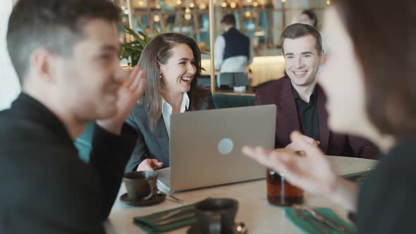 Group of Suit Wearing Colleagues Discussing Working Situation Sitting at Table in Cafe with Laptop alt