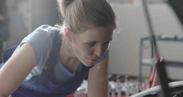 Professional female mechanic working in the auto repair shop, she is repairing a car