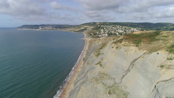 Aerial tracking above the Jurassic coast toward the village of Charmouth, Dorset. Cliffs, sea and th alt