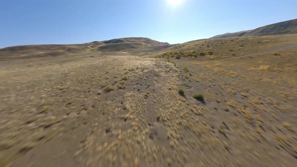 FPV Sports Drone Shot Sunny Panorama Hilly Desert Terrain Yellow Dry Structure Sun Light Blue Sky alt