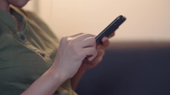 Asian woman using smartphone checking social media while sitting on a sofa.