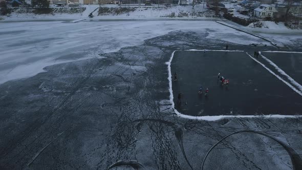 Drone Flight Over a Frozen Lake Where Children Train and Play Hockey Near the Shore on a Cloudy Day