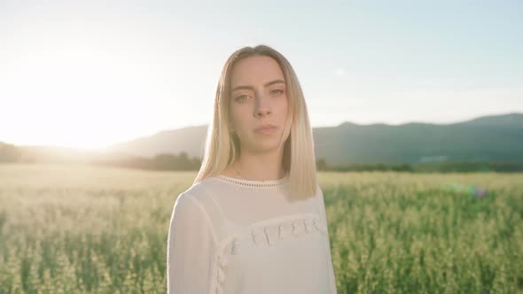 Attractive Caucasian girl posing in front of camera in rural farm field with sunset in background. alt