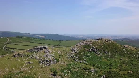 Wide shot aerial tracking forward upwards above Sharps Tor to reveal a wide expanse of countryside, alt