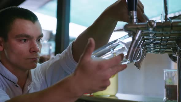 Professional Bartender Pours Fresh Cool Light Draft Beer Into a Glass Using Pour From Keg alt