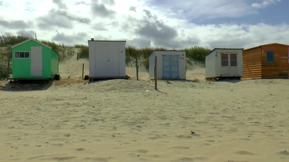 Several beach houses with different colors and shapes side by side on the beach of Texel. alt