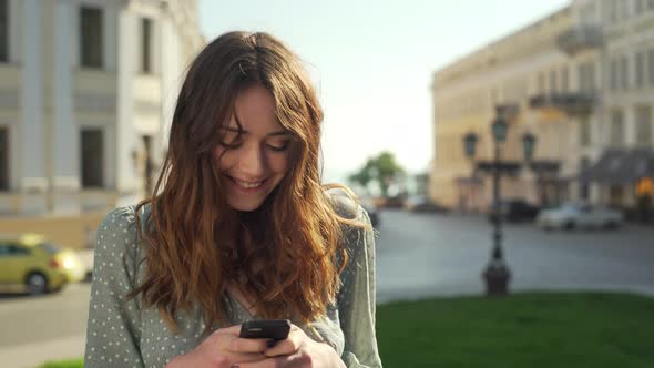 Portrait of Seductive Social Woman Wearing Dress Smiling and Holding Mobile Phone While Walking alt