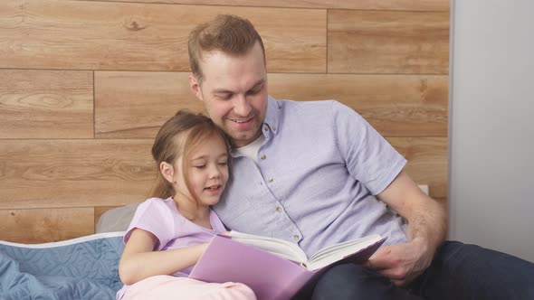 Handsome Caucasian Father Hold Story Book Reading Teaching Daughter Little Girl in Bedroom