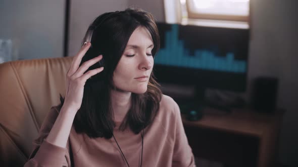 A beautiful girl with headphones listens to music in a chair at the computer, dances.