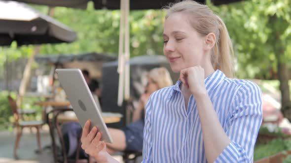 Online Video Chat on Tablet by Young Woman Sitting in Cafe Terrace alt