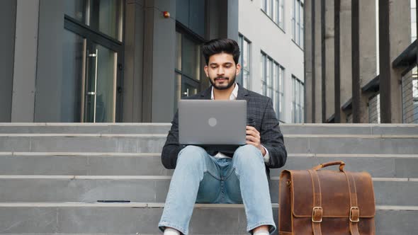 Successful Muslim Man Working on Laptop on Stairs Outdoors alt