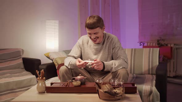 A Young Man at Home Cleans Dishes for a Special Tea Ceremony with a Towel, Smiles and Talks To a alt
