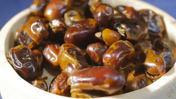 Brown Turkish Sweet Dates in a Wooden Bowl Closeup Rotate on a Blue Solid Background