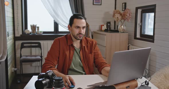 A Young Handsome Male Photographer and Videographer Works at Home on a Laptop