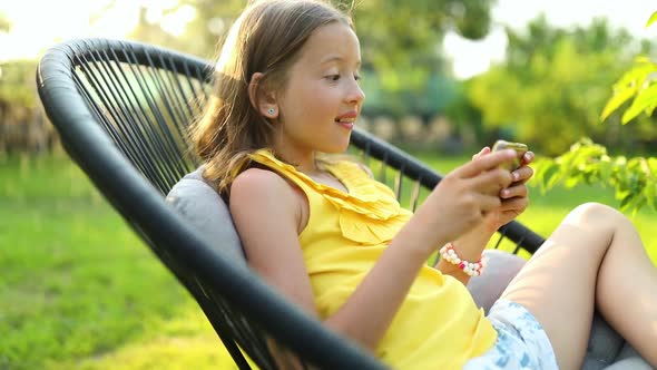 Happy kid girl playing game on mobile phone in the park outdoor