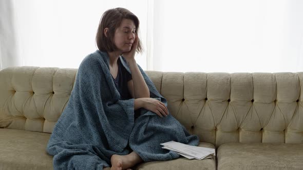 Distraught woman sitting on couch wrapped in blanket alt