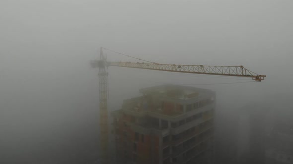 Birds eye view on tower crane in fog standing next to residential building. alt