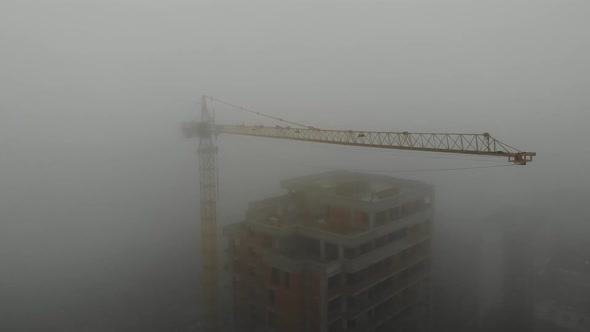 Birds eye view on tower crane in fog standing next to residential building.