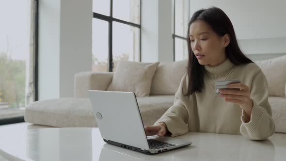 A Young Asian Woman Holding a Credit Card and Using a Laptop alt