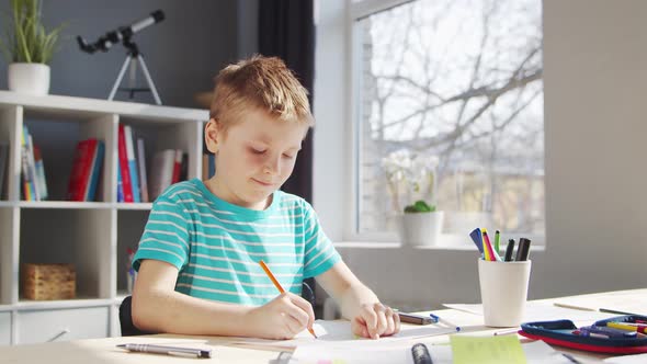 Boy is Doing  Homework at the Table. Cute Child is Learning at Home. alt
