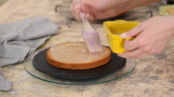 Unrecognizable female confectioner hand soaks sponge cake with sweet caramel syrup alt
