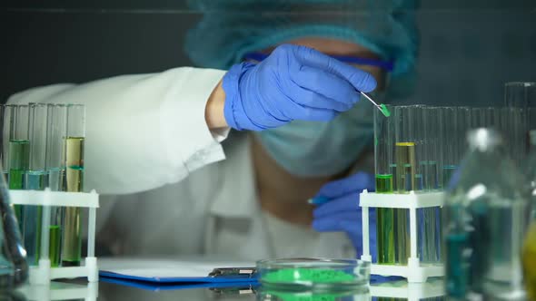 Left-Handed Researcher Adding Green Powder to Tube and Making Notes, Experiment alt