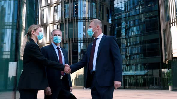 Businessmen and Businesswoman in Medical Mask Meet a Colleague Also Wearing a Mask and Shake Hands